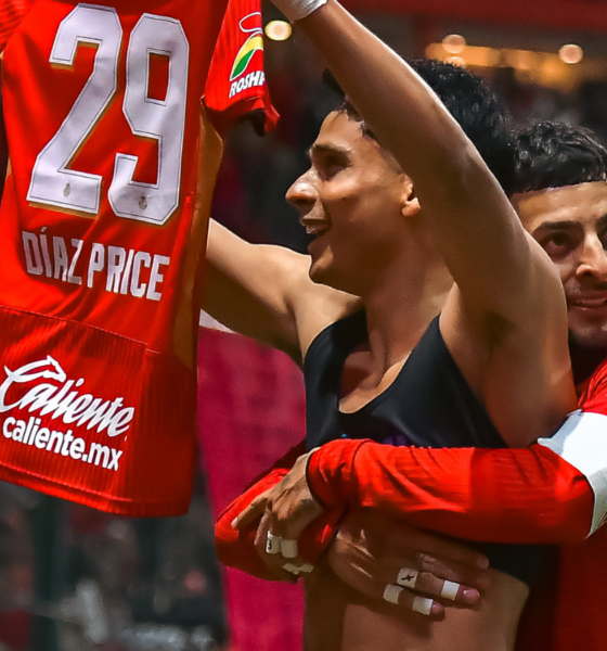 Two celebrating players embrace on the field, one lifting a red jersey with number 29 and sponsor branding visible, crowd in the background.