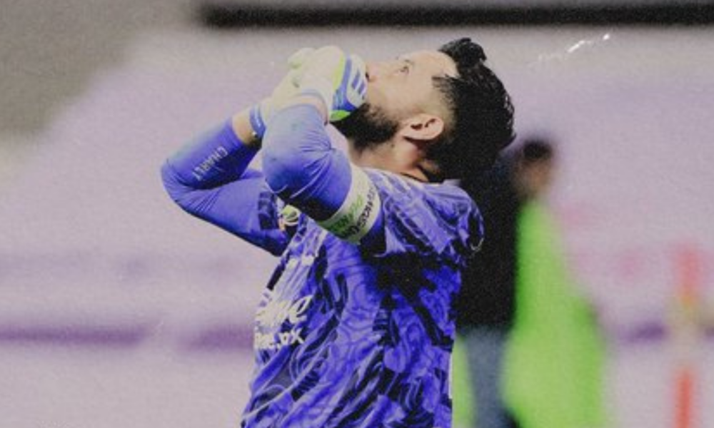 Soccer goalkeeper in a blue kit with gloves, hands on head in disbelief or frustration on the field