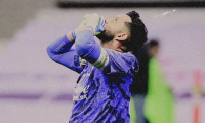 Soccer goalkeeper in a blue kit with gloves, hands on head in disbelief or frustration on the field