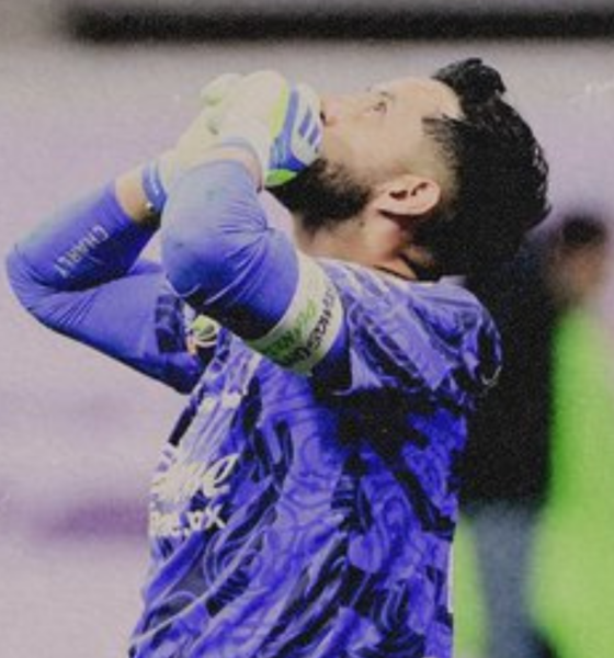 Soccer goalkeeper in a blue kit with gloves, hands on head in disbelief or frustration on the field