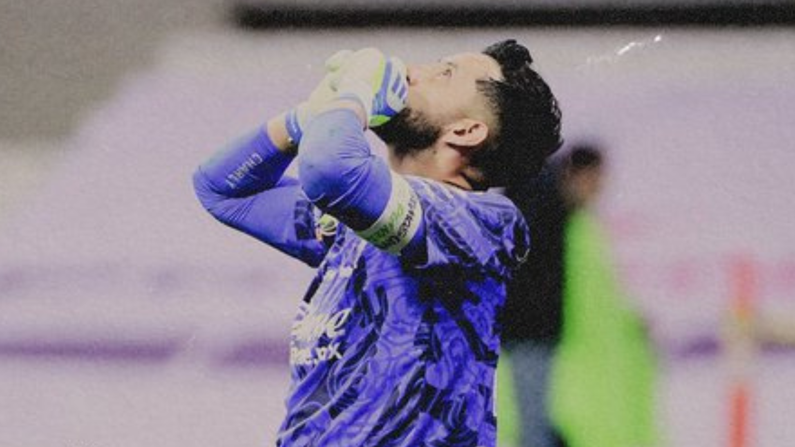 Soccer goalkeeper in a blue kit with gloves, hands on head in disbelief or frustration on the field