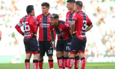 Five soccer players in red-and-black striped uniforms huddle on a green pitch during a match.