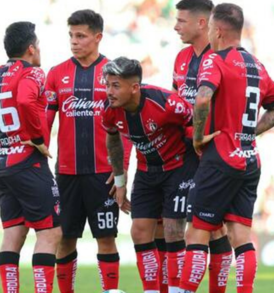 Five soccer players in red-and-black striped uniforms huddle on a green pitch during a match.