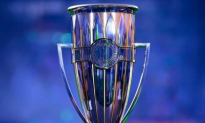 Shiny silver trophy with blue background, central circular medallion and two handles on sides.