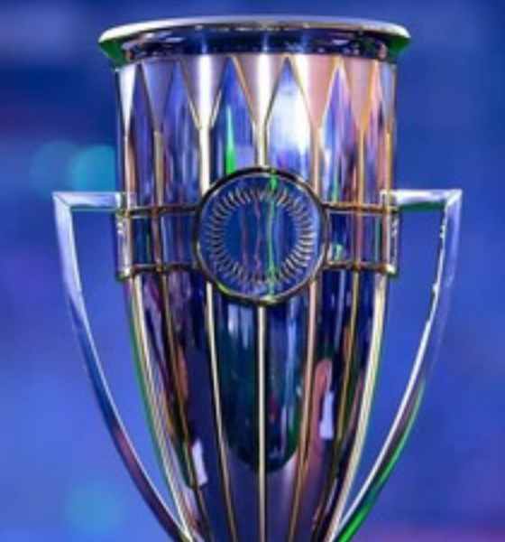 Shiny silver trophy with blue background, central circular medallion and two handles on sides.