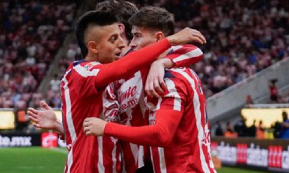 Two soccer players in red-and-white striped uniforms embrace in celebration on the field.