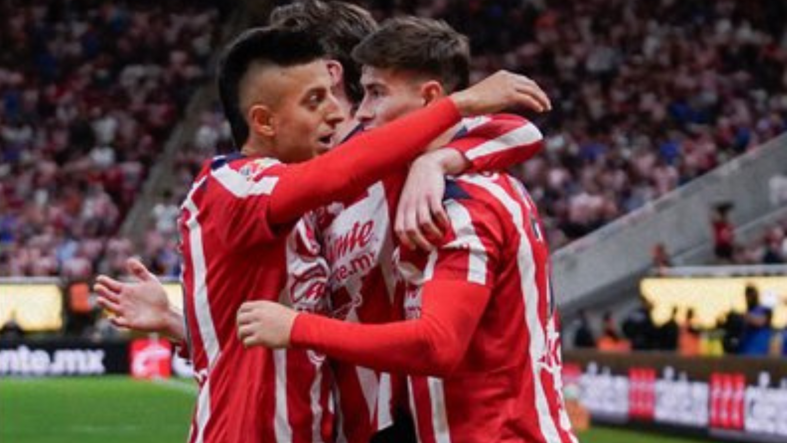 Two soccer players in red-and-white striped uniforms embrace in celebration on the field.