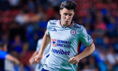 Soccer player in a white Cruz Azul jersey running on the field during a match, crowd in the background.