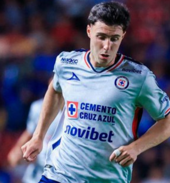 Soccer player in a white Cruz Azul jersey running on the field during a match, crowd in the background.
