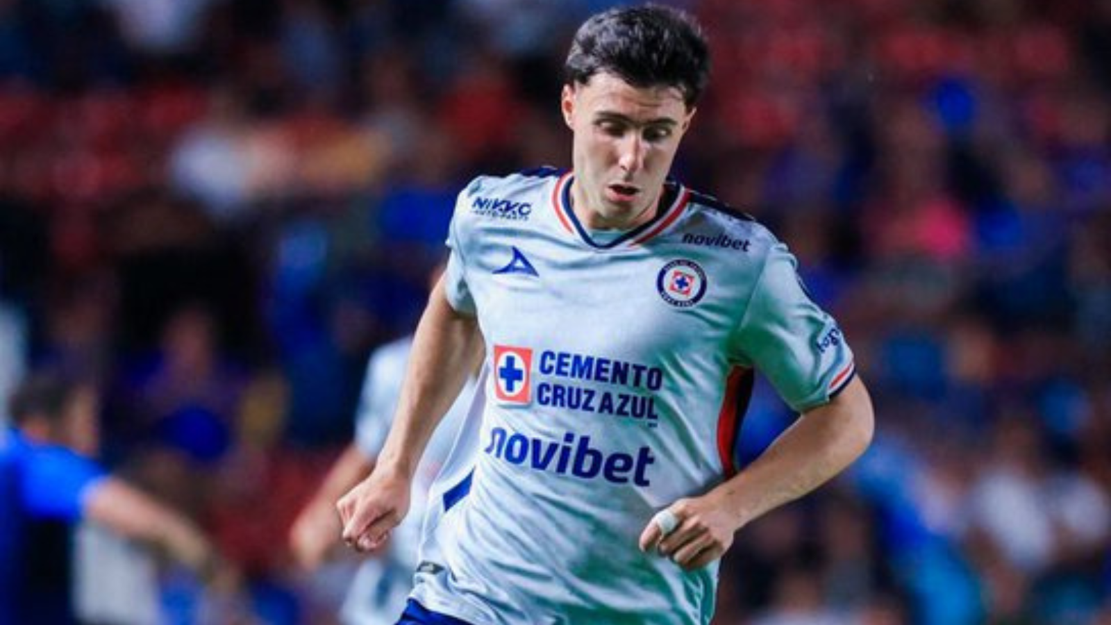 Soccer player in a white Cruz Azul jersey running on the field during a match, crowd in the background.