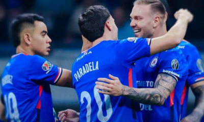 Soccer players in blue uniforms celebrate with arms around each other on the field after a play or goal.”