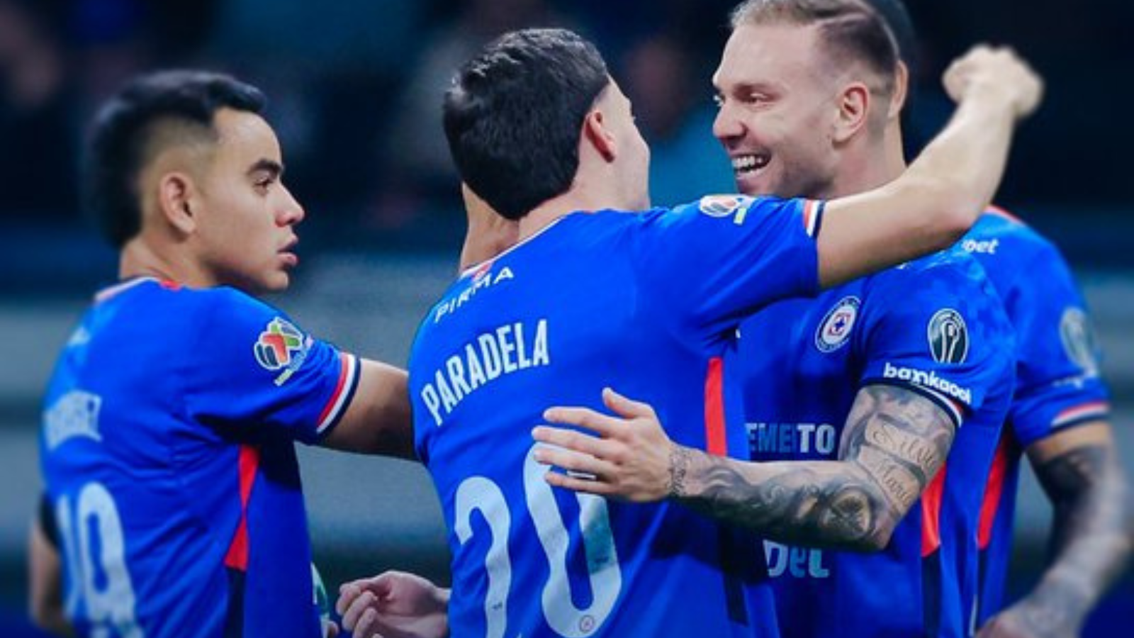 Soccer players in blue uniforms celebrate with arms around each other on the field after a play or goal.”