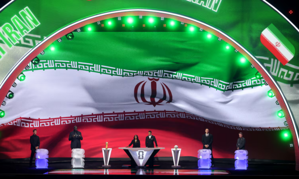 Large curved stage with Iran flag backdrop; six people stand at podiums with trophies during an awards ceremony.