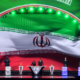 Large curved stage with Iran flag backdrop; six people stand at podiums with trophies during an awards ceremony.