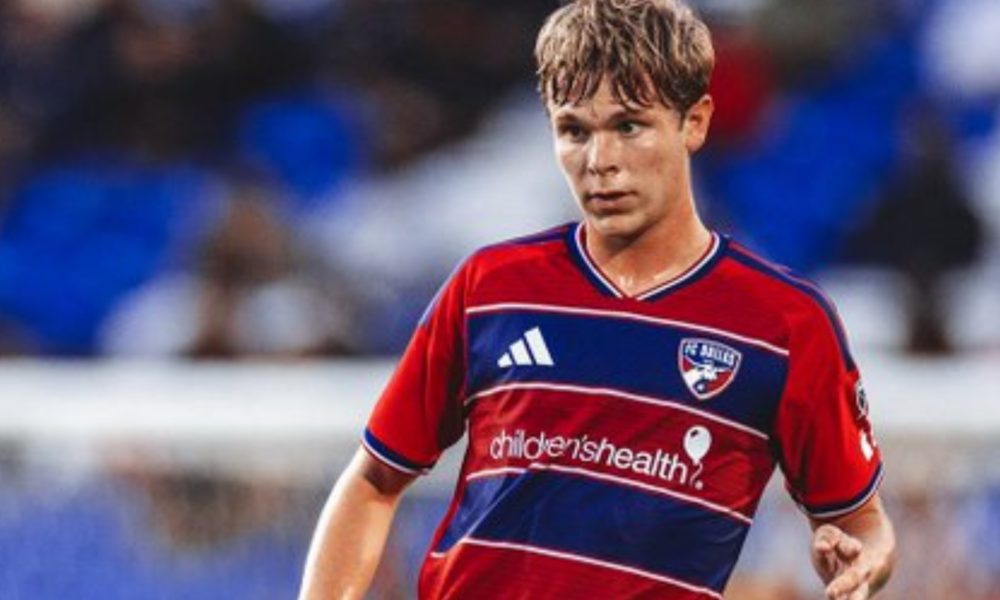 Young male soccer player in a red-and-blue jersey dribbling on the field; sponsor 'children's health' visible on the chest.