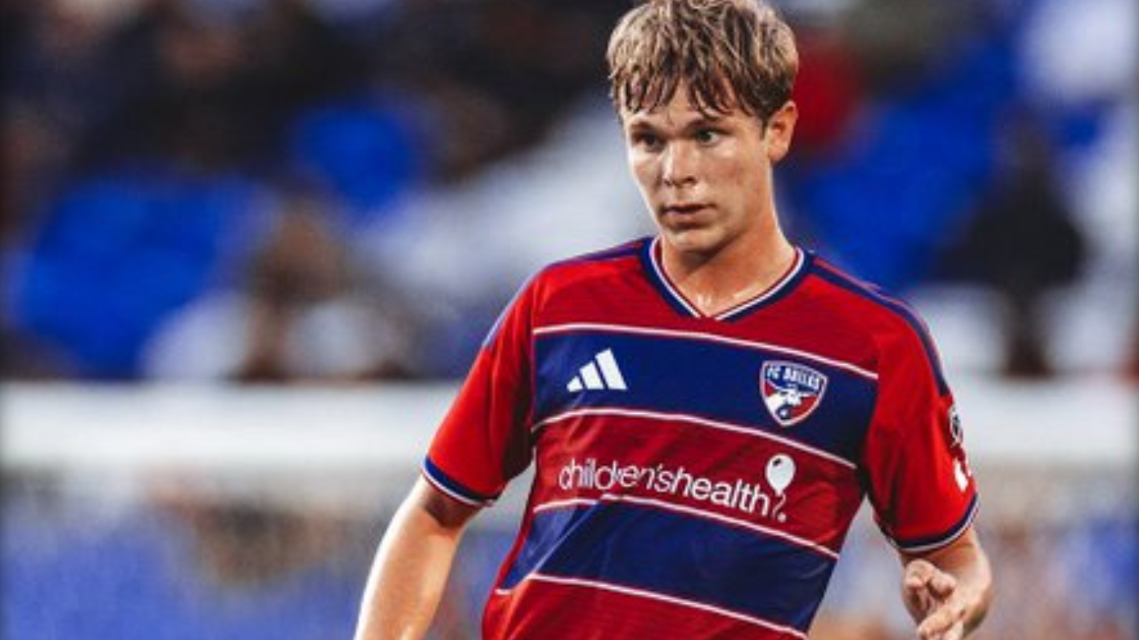 Young male soccer player in a red-and-blue jersey dribbling on the field; sponsor 'children's health' visible on the chest.