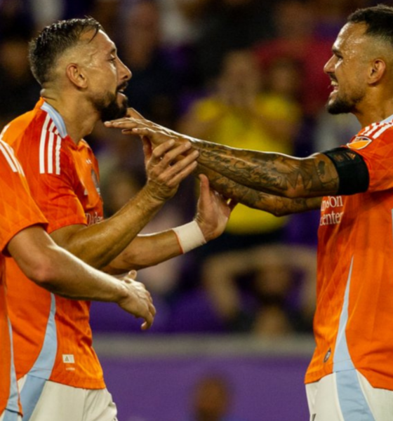 Soccer players in orange jerseys celebrate with a joint high-five on the pitch during a match.