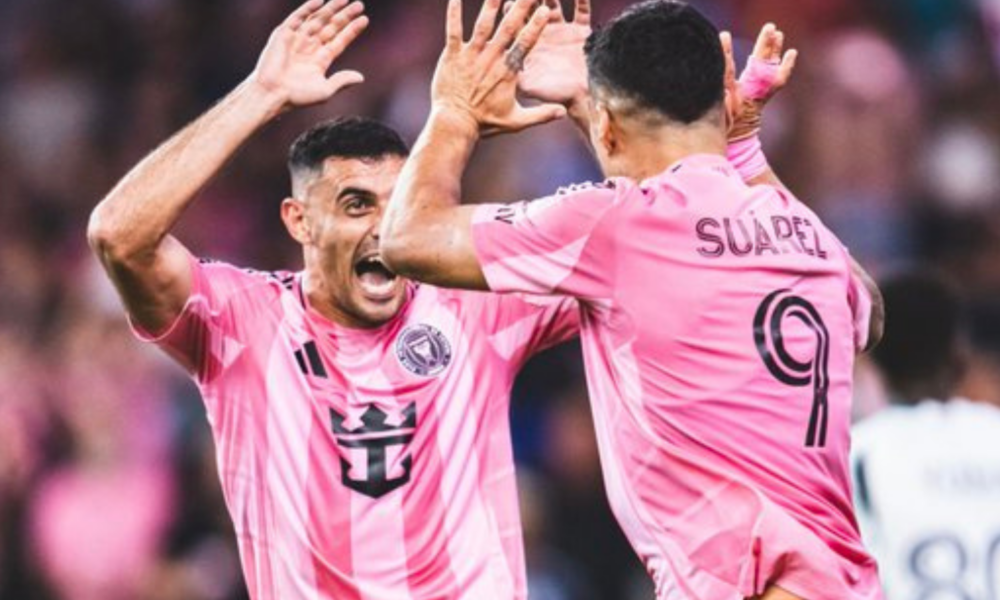 Two soccer players in pink jerseys celebrate with a high-five on the field.