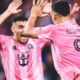 Two soccer players in pink jerseys celebrate with a high-five on the field.