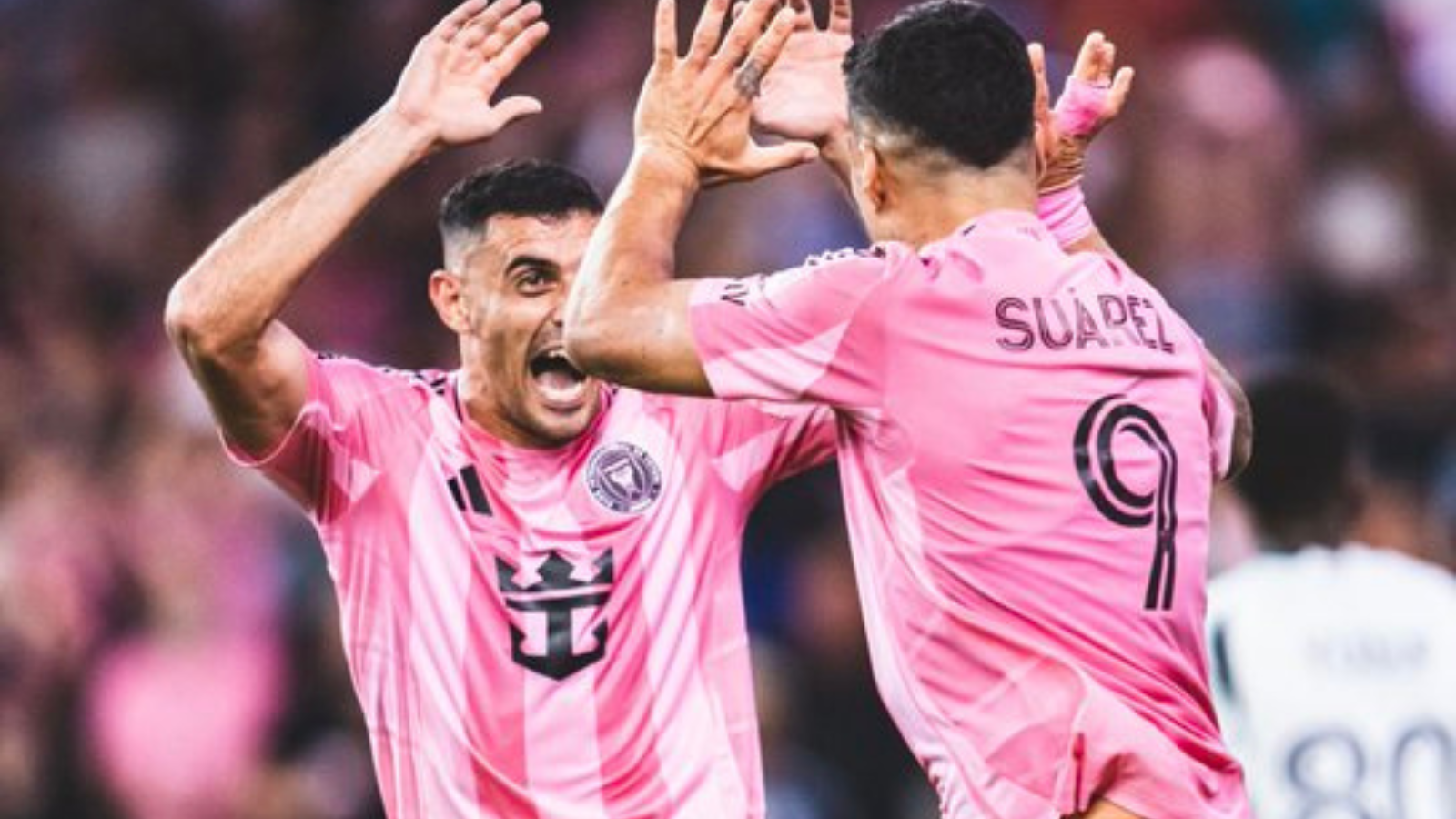 Two soccer players in pink jerseys celebrate with a high-five on the field.