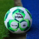 Soccer ball with Volt branding resting at the edge of green grass and blue artificial turf.