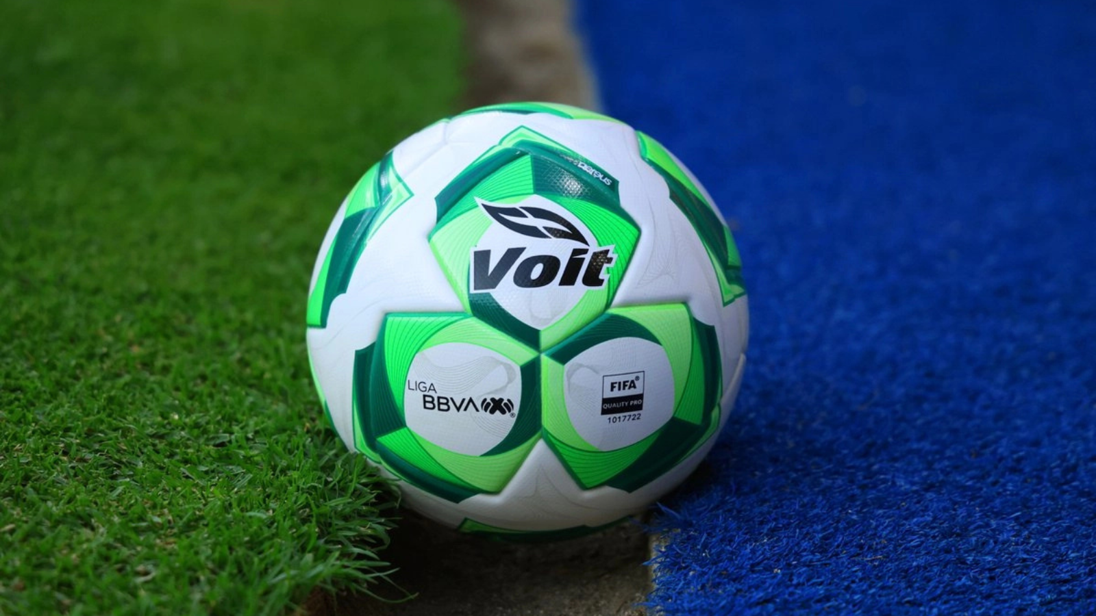 Soccer ball with Volt branding resting at the edge of green grass and blue artificial turf.