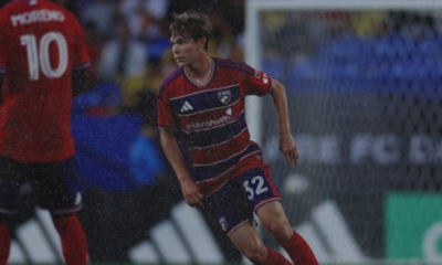 Soccer player in a red and blue striped kit sprinting on the pitch during a match, jersey number 32.