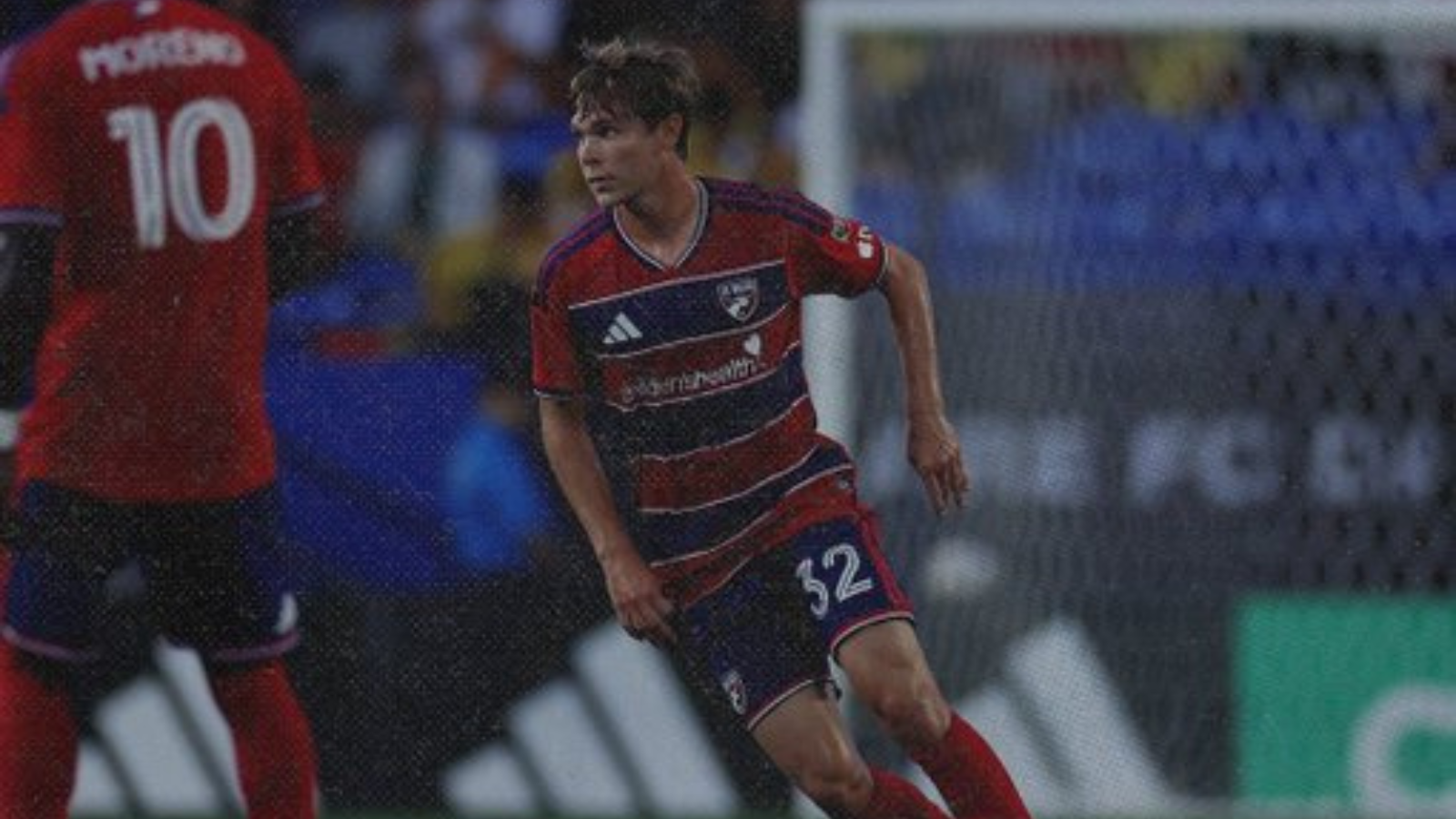 Soccer player in a red and blue striped kit sprinting on the pitch during a match, jersey number 32.