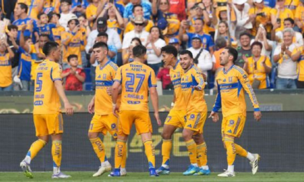 Soccer players in yellow uniforms celebrate on the field with cheering fans behind them in yellow and blue.