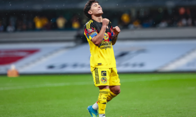 Soccer player in a yellow kit celebrating with clenched fists on a rain-soaked pitch.