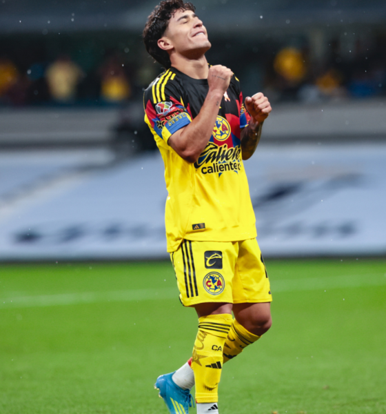 Soccer player in a yellow kit celebrating with clenched fists on a rain-soaked pitch.