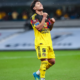 Soccer player in a yellow kit celebrating with clenched fists on a rain-soaked pitch.