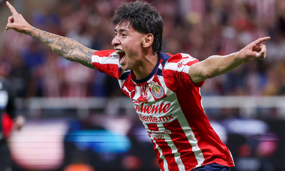 Soccer player in red-and-white striped jersey celebrating with arms outstretched and mouth open in a stadium
