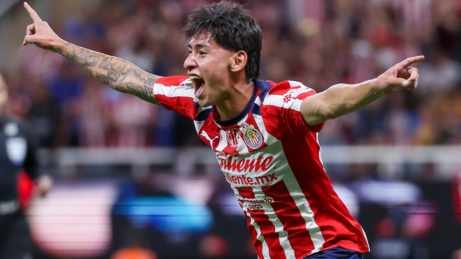 Soccer player in red-and-white striped jersey celebrating with arms outstretched and mouth open in a stadium