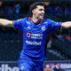 Cruz Azul footballer in a blue kit celebrates with arms outstretched on the field.