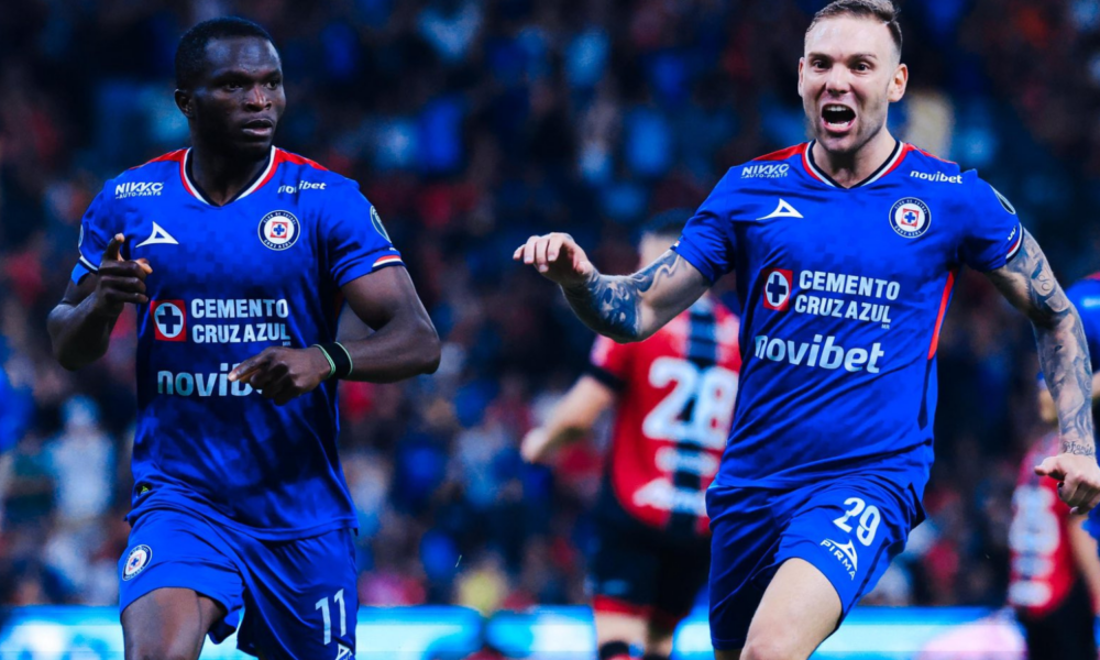 Two Cruz Azul soccer players in blue jerseys celebrate on the pitch during a match.