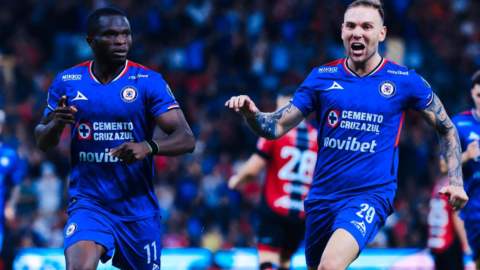 Two Cruz Azul soccer players in blue jerseys celebrate on the pitch during a match.
