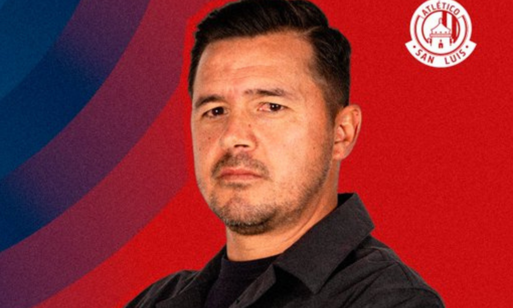 Portrait of a man in a black shirt against a red and blue backdrop with the Atlético San Luis logo in the top-right corner