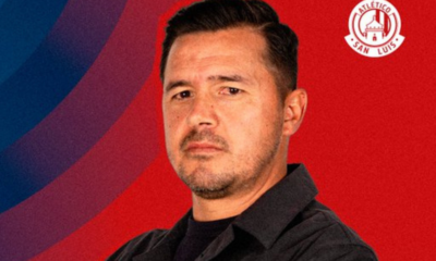 Portrait of a man in a black shirt against a red and blue backdrop with the Atlético San Luis logo in the top-right corner