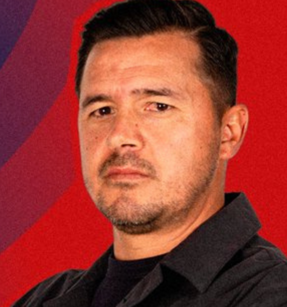 Portrait of a man in a black shirt against a red and blue backdrop with the Atlético San Luis logo in the top-right corner