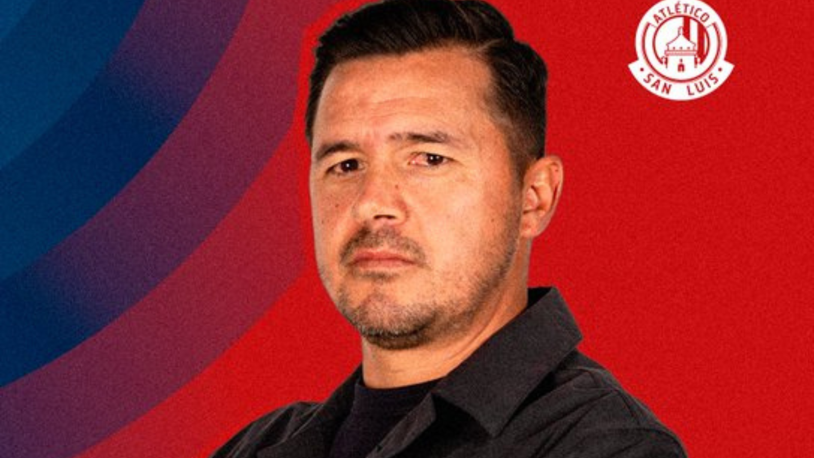 Portrait of a man in a black shirt against a red and blue backdrop with the Atlético San Luis logo in the top-right corner