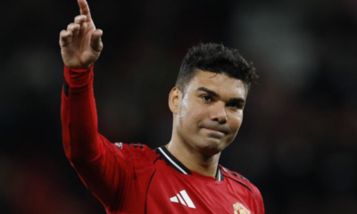 Soccer player in a red Manchester United jersey raises his right index finger in the air, looking forward.
