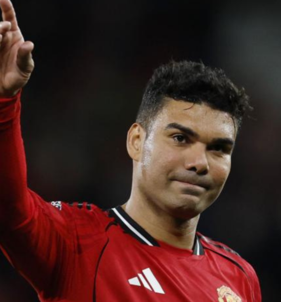 Soccer player in a red Manchester United jersey raises his right index finger in the air, looking forward.