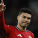 Soccer player in a red Manchester United jersey raises his right index finger in the air, looking forward.