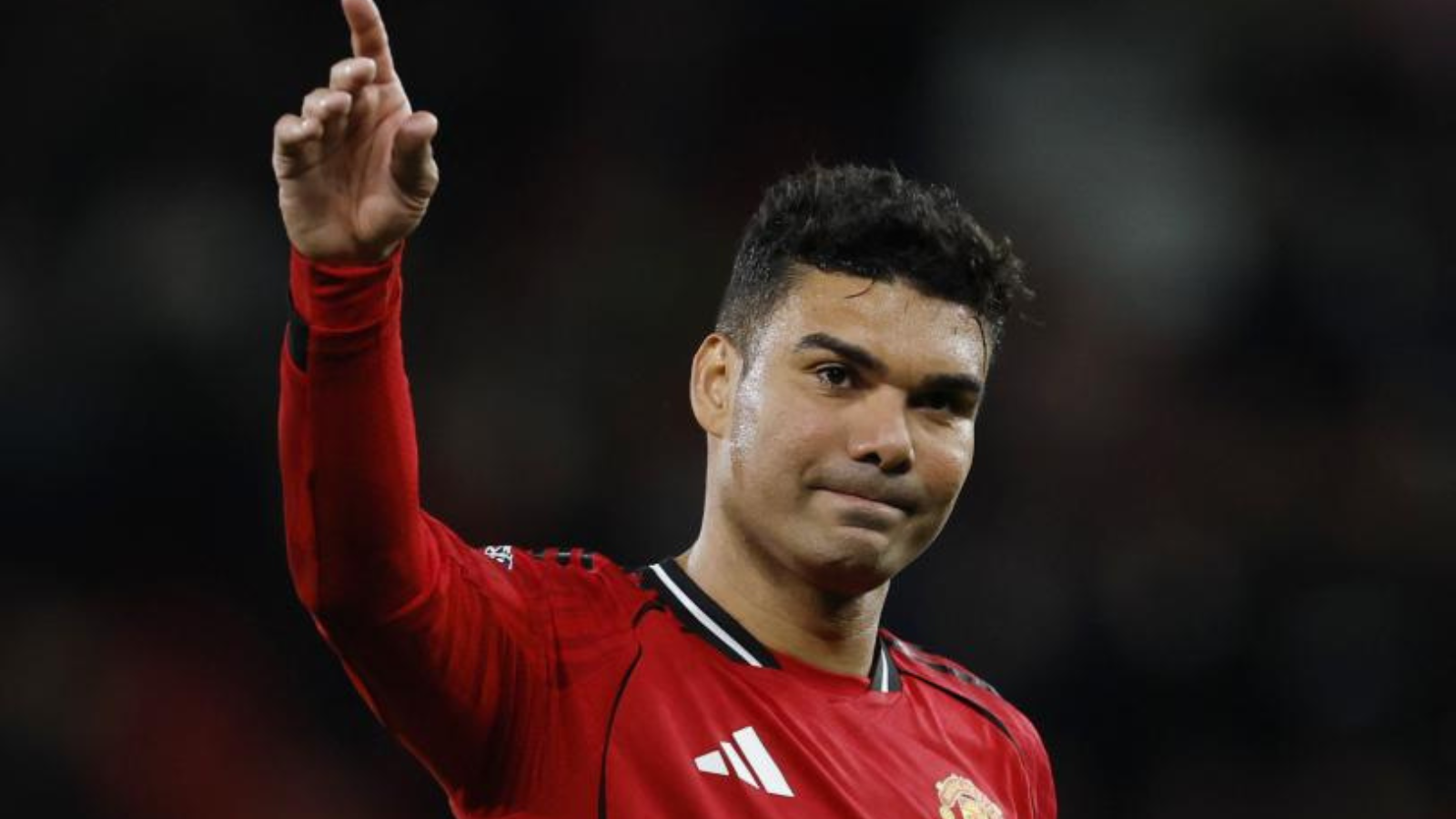 Soccer player in a red Manchester United jersey raises his right index finger in the air, looking forward.