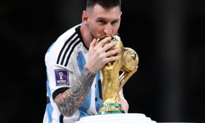 Messi kissing the FIFA World Cup trophy while holding it close in an Argentina jersey with the tournament patch visible on the sleeve
