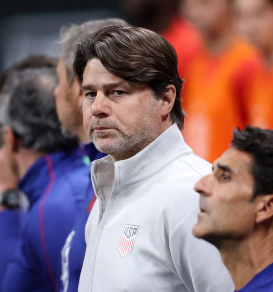 Man in a white USA jacket with crest, standing on the sidelines during a lineup.