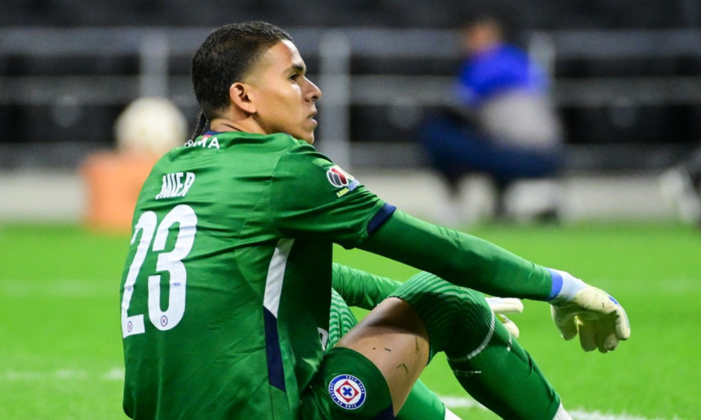 Soccer goalkeeper in a green kit with number 23 sits on the grass, knees up, during a match.