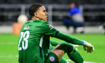 Soccer goalkeeper in a green kit with number 23 sits on the grass, knees up, during a match.
