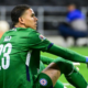 Soccer goalkeeper in a green kit with number 23 sits on the grass, knees up, during a match.